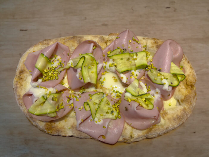 Roman pinsa, variant of the classic Italian pizza topped with mortadella, stracciatella and lamb's lettuce and pistachios