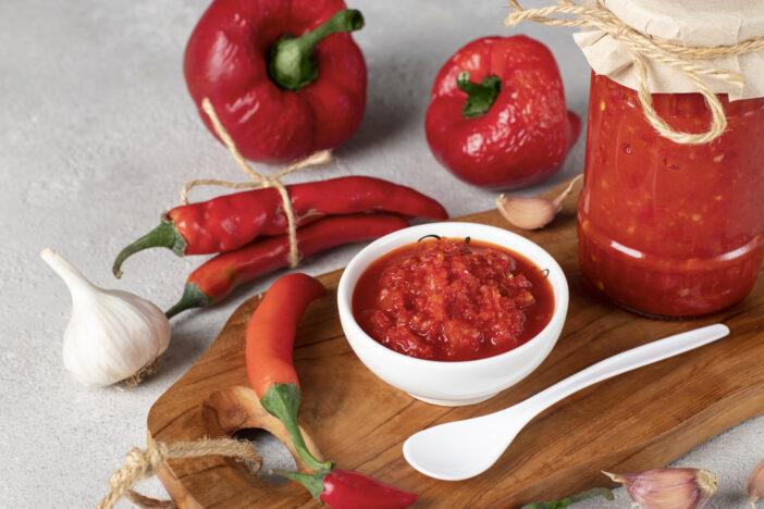 Traditional sauce adjika with hot chili pepper, paste harissa in white bowl on wooden board