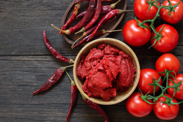 Traditional turkish chili pepper and tomato paste in bowl or spoon with dried peppers and fresh tomatoes on table