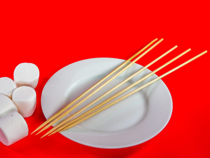 Bamboo skewers on white plate with marshmallows on red background