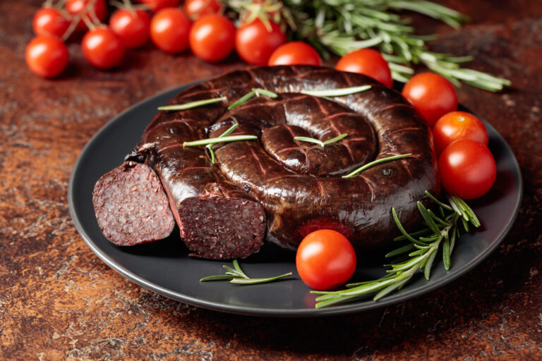 Black pudding or blood sausage with rosemary and tomatoes on a black plate.