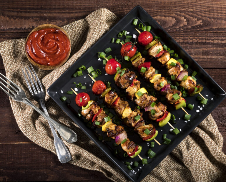 Grilled chicken skewers with spices and vegetables in a pan on a wooden background. Top view.