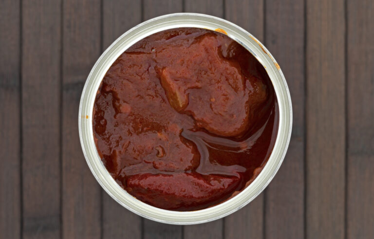 Top view of an opened can of chipotle peppers in an adobo sauce atop a brown wood place mat.