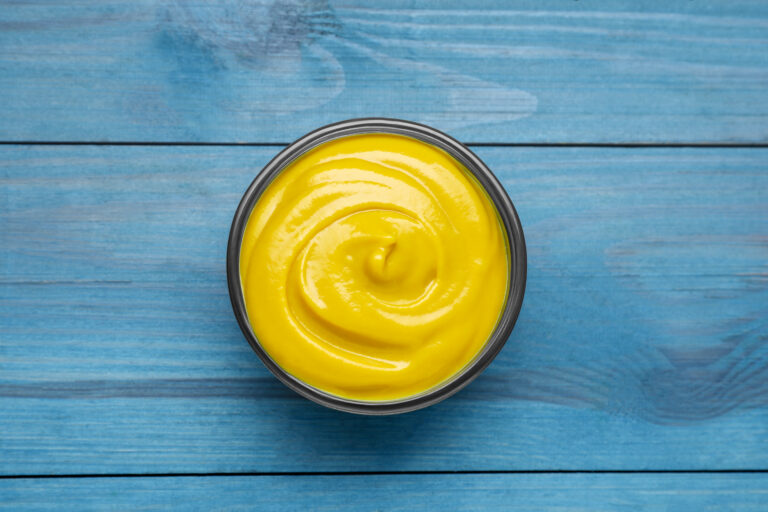 Sauce bowl with delicious mustard on light blue wooden table, top view