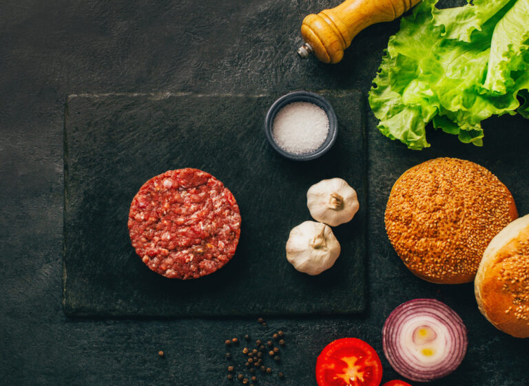 top view of hamburger ingredients raw meat buns vegetables condiments on dark table with free space for text