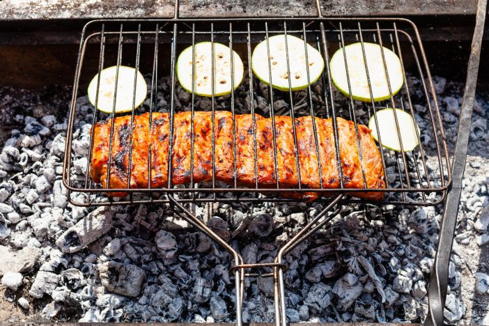 cooking pork ribs marinated in sauce with sliced zucchini vegetable in outdoor charcoal grill