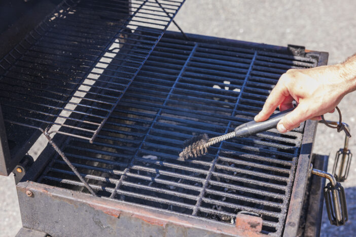 Close up view of man hand using brush to clean grill for cooking meat.