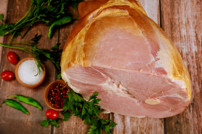 Whole pork ham with fresh parsley, hot pepper and salt on wooden rustic table.