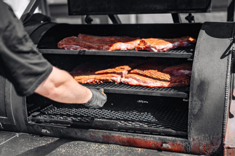 Chef hand cooking grilled pork meat in BBQ smoker.