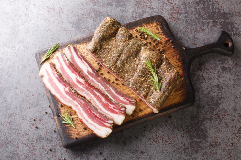 Dry-cured pork belly bacon with spices and rosemary close-up on a wooden board on the table. horizontal top view from above