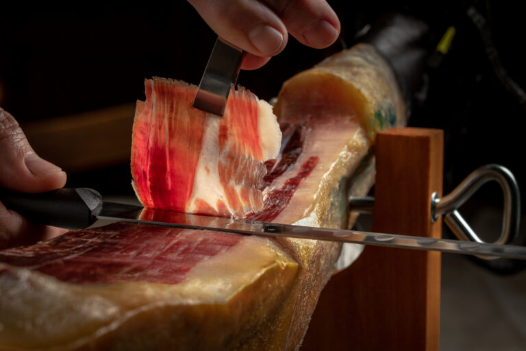 Close up of cutter gourmet hands slicing acorn fed iberian ham. Typical and traditional spanish delicatessen pork food.