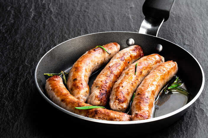 Delicious  pork chipolatas sausages in a frying pan on black stone background