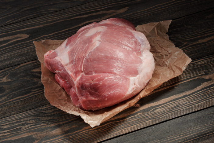 A piece raw pork shoulder. Pork tenderloin on paper on a dark  table