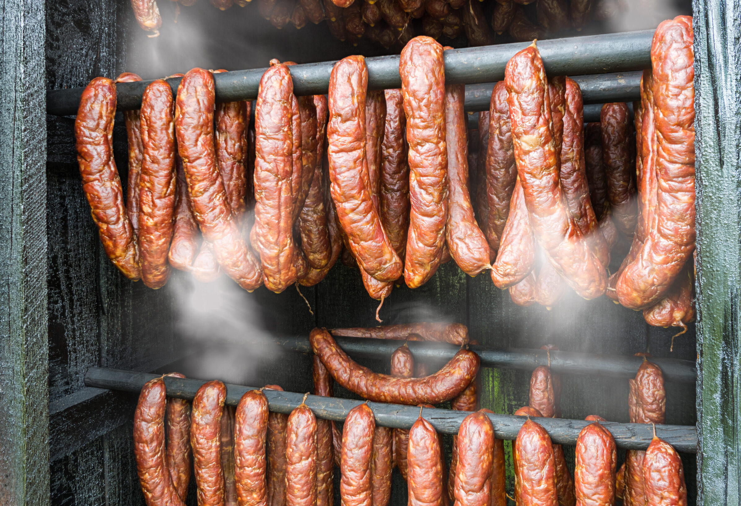 Closeup of hot smoky sausages from pork and beef meat hanging inside homemade smokery. Making tasty savoury charcuterie in smokehouse