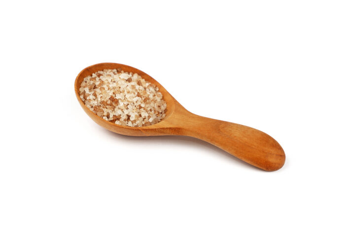 Close up one wooden scoop spoon full of brown smoked Danish salt isolated on white background, high angle view