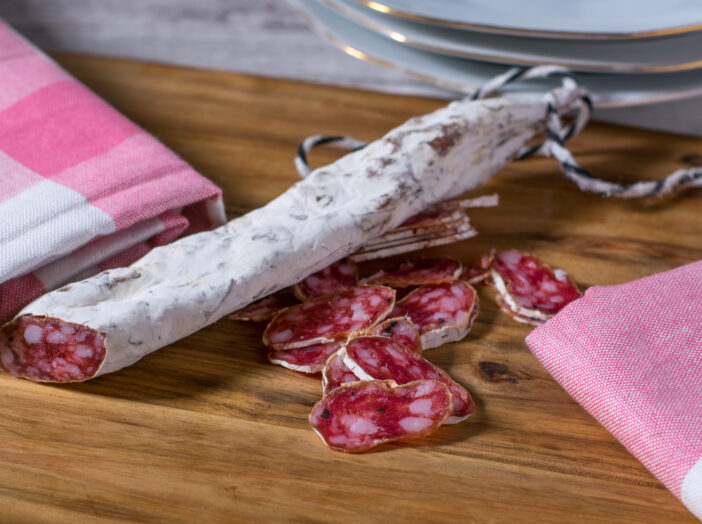 spanish salami air dried with truffle and white mold served on a rustic wooden board on kitchen table. origainal and traditional delicacy from Spain