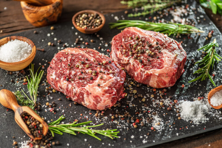 Raw Ribeye steaks with salt and herbs on grey board. Top view.