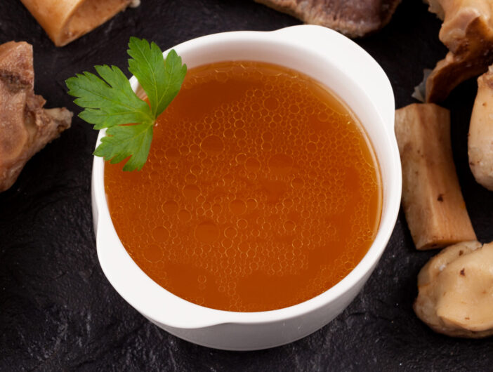 Bone broth on a stone surface next to boiled beef bones. Selective focus, copy space.