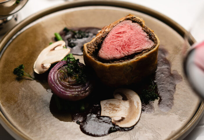 Beef Wellington with mushrooms, french fries and red wine sauce on a white tablecloth