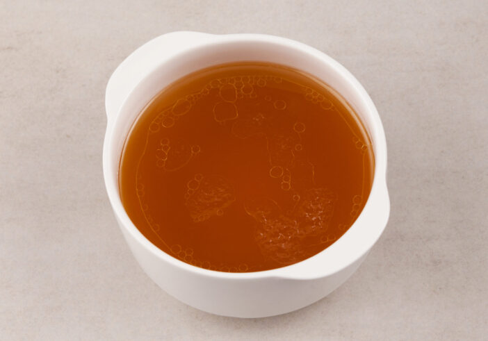 Beef bone broth  in white bowl on a stone surface. Healthy beverage with natural collagen. Selective focus, copy space.