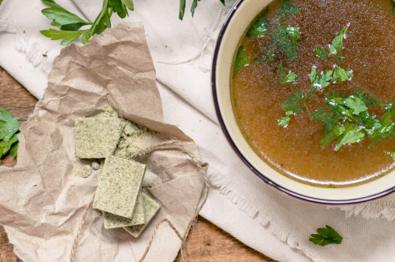 Bouillon cubes next to a bowl of broth. Parsley close, top view