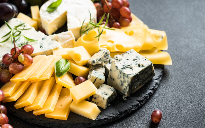 Cheese platter with craft cheese assortment and grape on slate board.