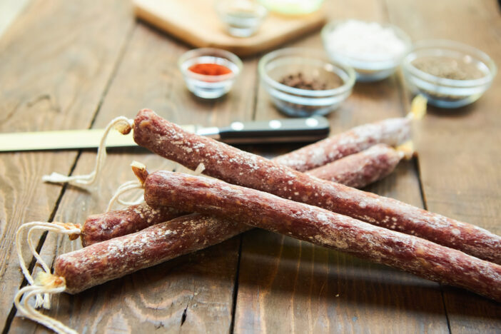 Smoked or cured sausage lies on a wooden table surrounded by spices. Meat production