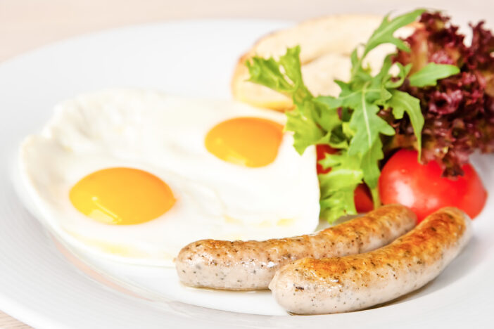 Fried eggs with sausages, tomatoes, rucola and lettuce