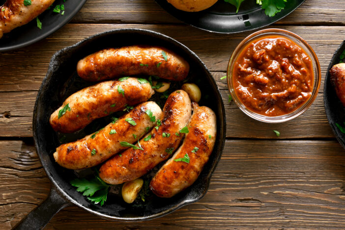 Fried sausages in frying pan over wooden background. Top view, flat lay