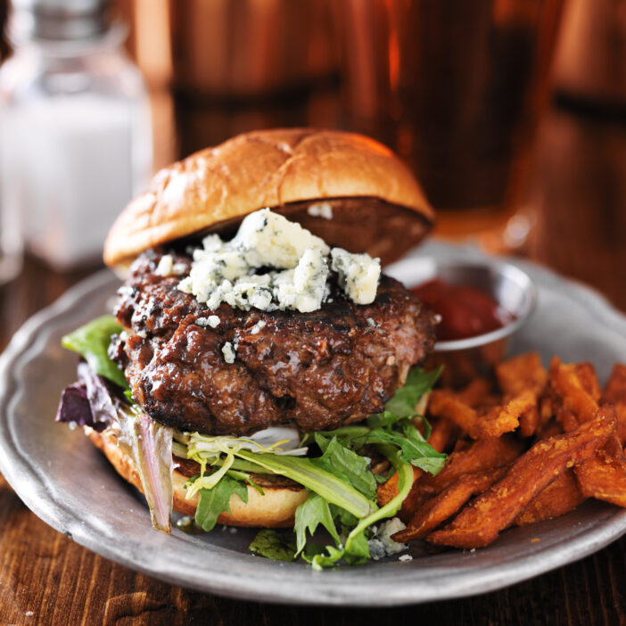 gourmet burger with blue cheese and sweet potato fries shot close upo in square composition.