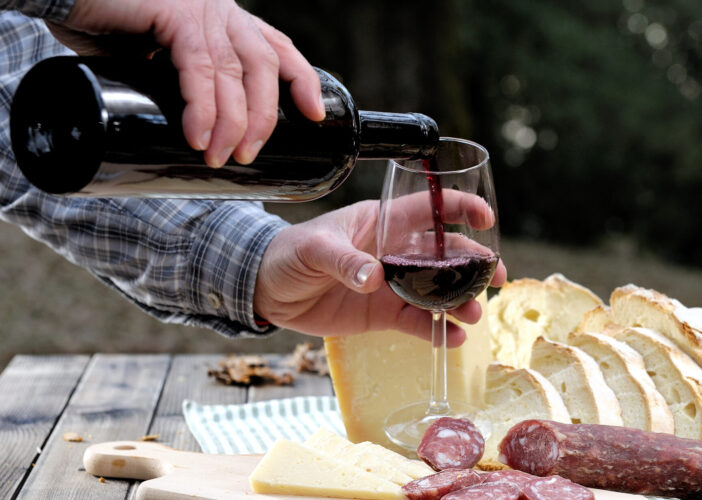 Hands that shed the wine into the chalice while eating in the countryside with bread, cheese and sausage.