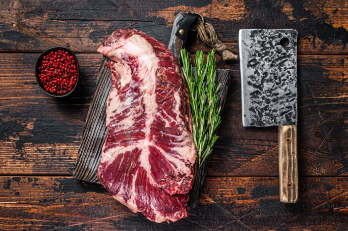 Hanging tender or hanger raw beef meat steak on butcher board with cleaver. Dark wooden background. Top View.