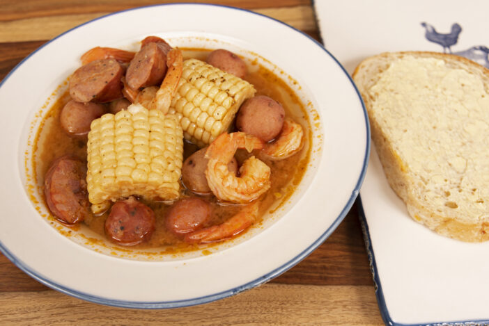 Homemade Cajun Shrimp Boil with corn, new potatoes, and andouille sausage with a slice of sourdough bread, served in a white bowl