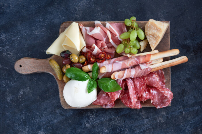 Italian antipasti wine snacks set. Brushettas, cheese variety, Mediterranean olives, pickles, Prosciutto di Parma with melon, salami and wine in glasses over black grunge background, top view