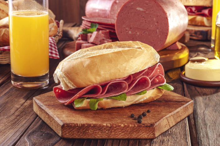 Mortadella sandwich with orange juice, butter and piece of mortadella on wood background