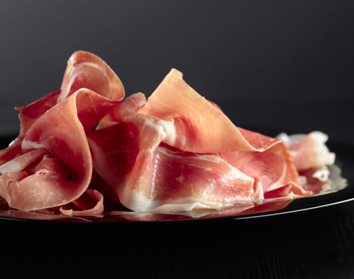 Italian prosciutto or Spanish jamon on a black plate.