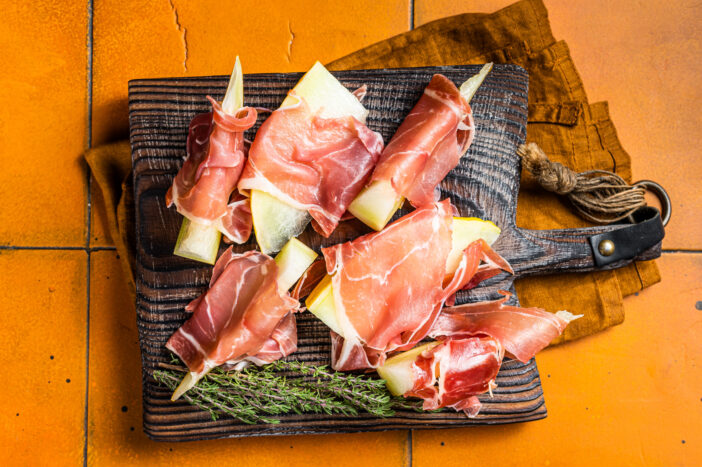 Prosciutto ham with slices of melon and fresh thyme. Orange background. Top view.