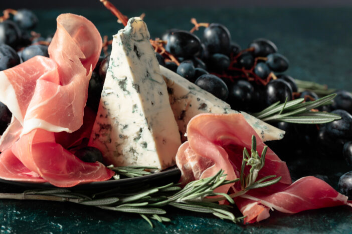 Prosciutto with blue cheese, grapes, and rosemary, on vintage background.