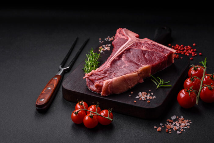 Raw juicy beef t-bone steak with salt, spices and herbs on a textured concrete background