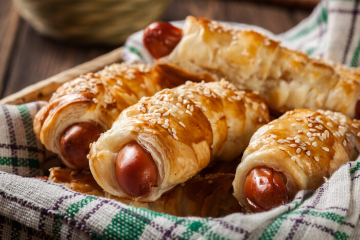 Rolled hot dog sausages baked in puff pastry in a wicker basket