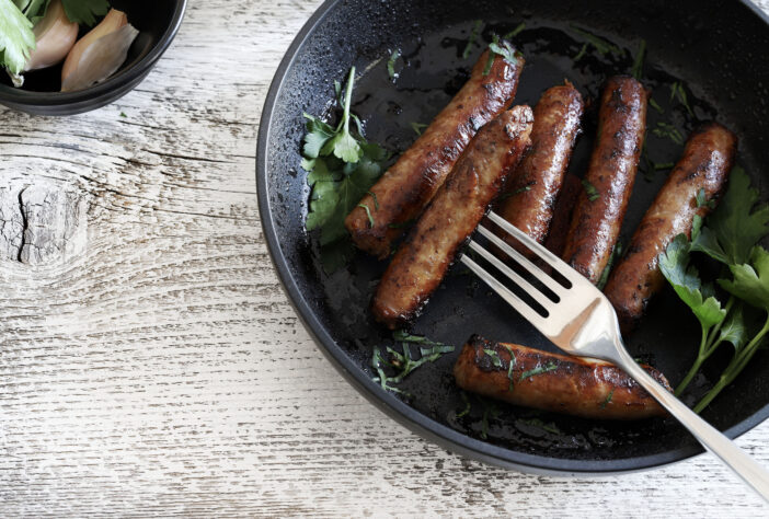 Tasty fried sausages in a frying pan over wooden background. Directly above. Copy space.