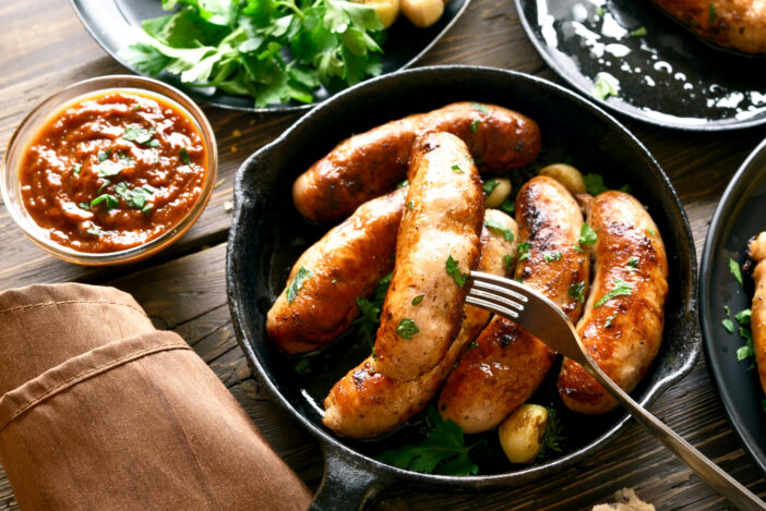 Tasty fried sausages in frying pan on wooden table. Close up view