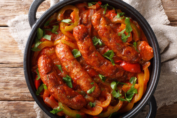 Traditional grilled sausages with multicolored peppers, onions and tomatoes close-up in a pan on the table.  horizontal top view from above