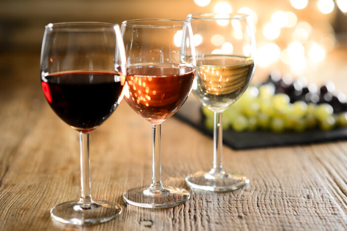 three glass of white red and rose wine with dim light in wooden restaurant table with a grape background