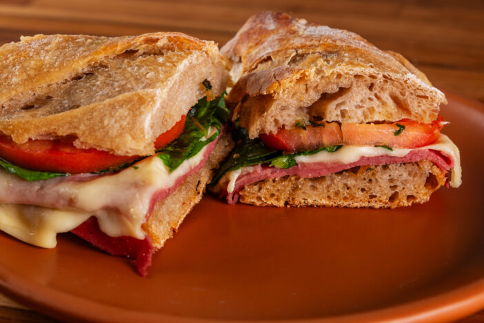 artisanal baguette sandwich with melted mozzarella, mortadella, arugula and tomato slices.