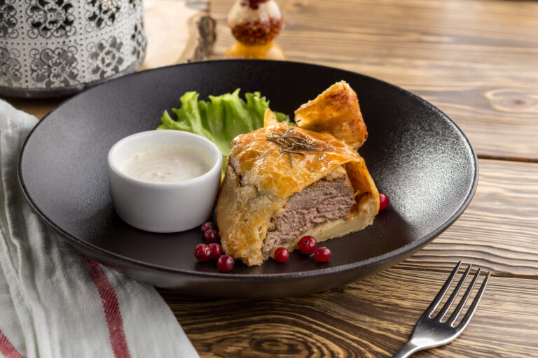 Beef wellington with cranberry and white sauce on wooden table side view