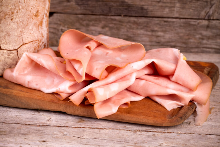 Slices of fresh mortadella and bread on wooden board.