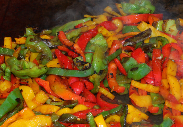 Yellow red and green peppers sizzling on the hot griddle of a street food truck cooking with spices and plenty of oil