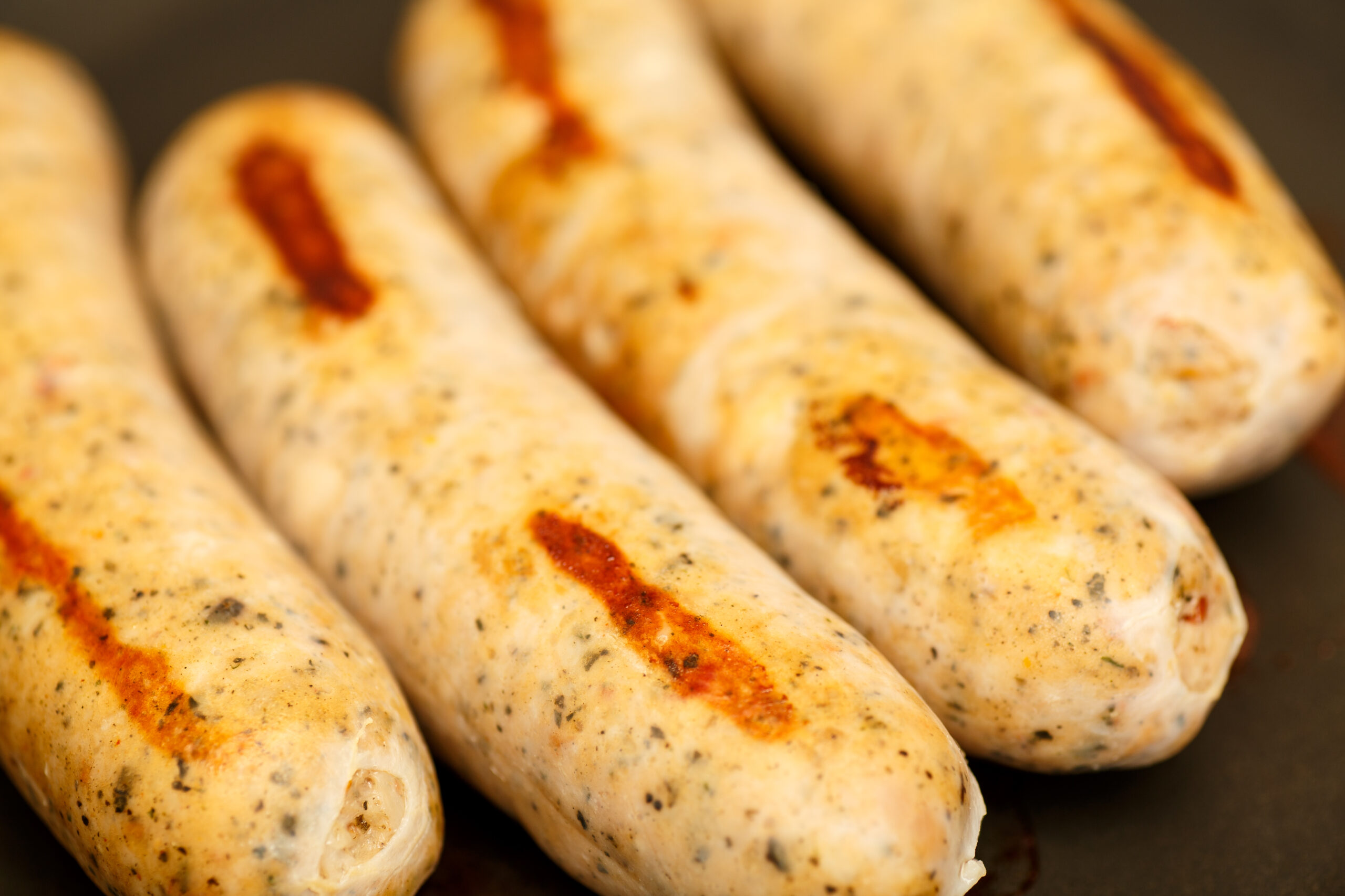 Four chicken sausages browning in a frying pan