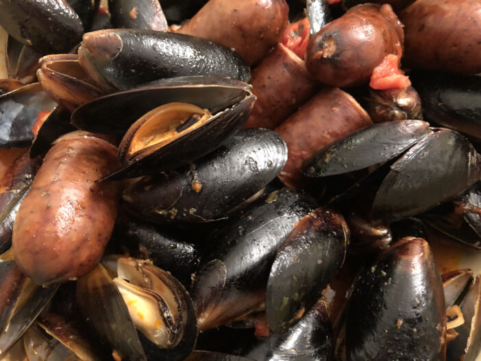 Closeup shot of cooked mussels and spicy andouille sausage cooked together in a tomato-based sauce